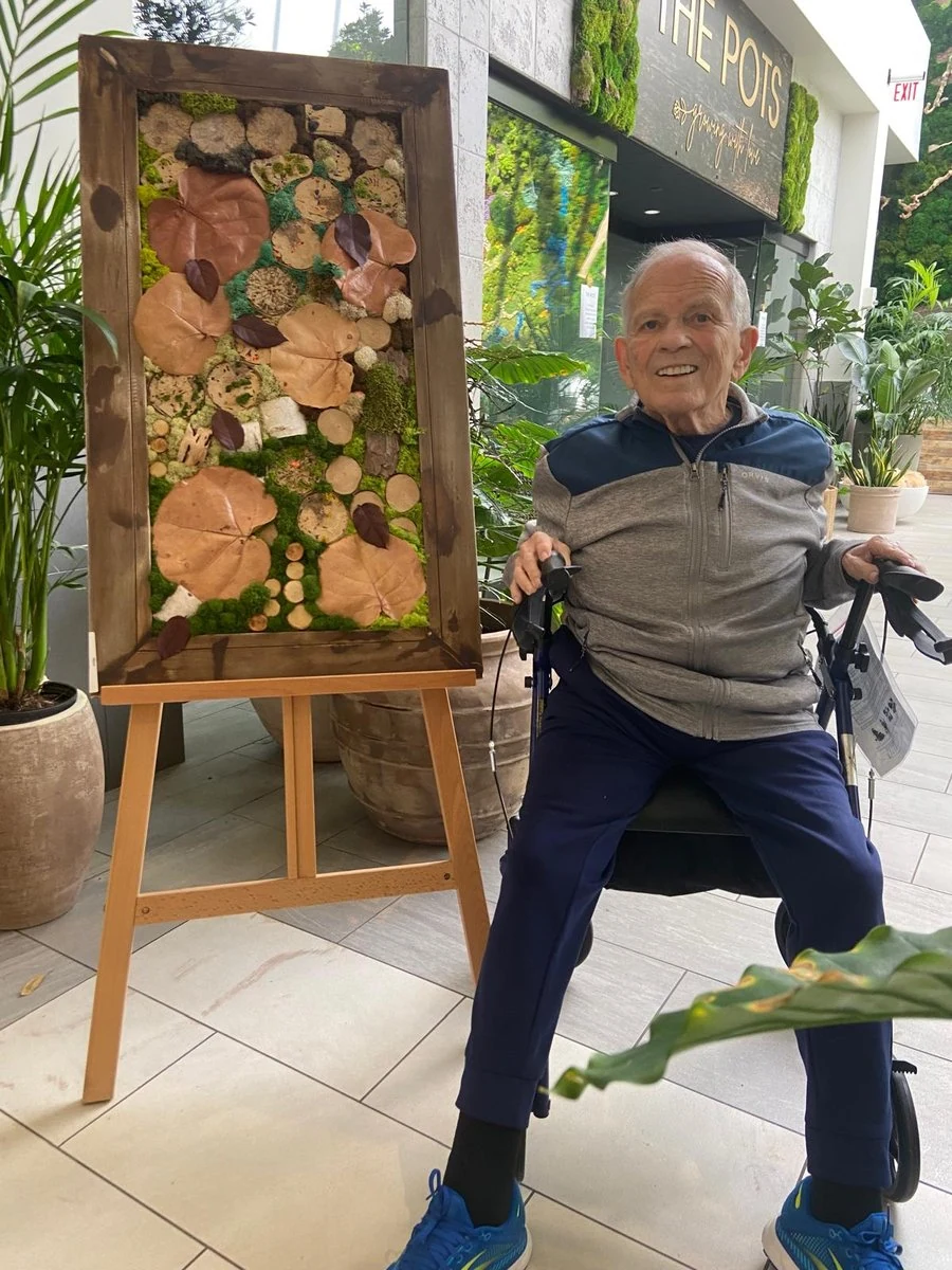 Un hombre mayor sonríe junto a un cuadro con plantas durante una salida.